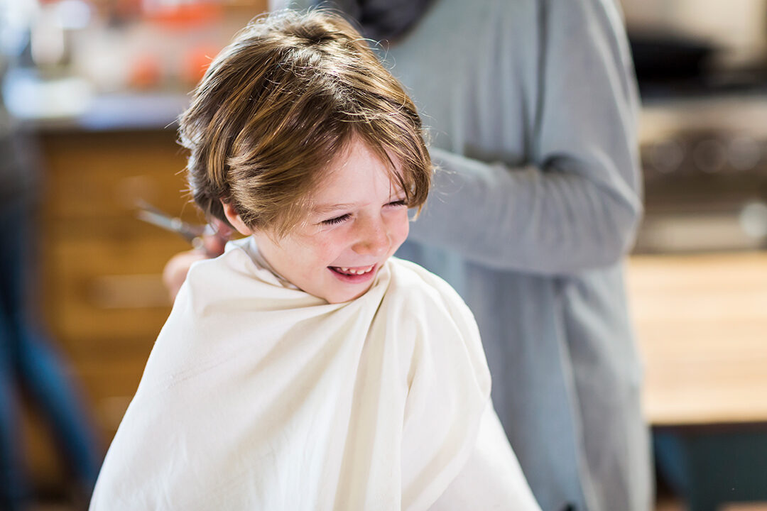 A six year old boy getting his hair cut at home by his mother