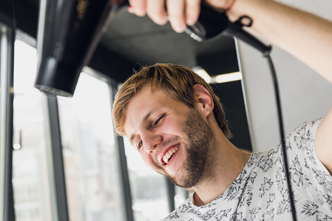 Portrait of happy hairdresser holding comb and blow dryer in salon.